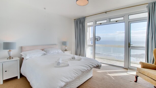Et hotelværelse med en stor seng, to sengeborde med lamper, en stol og en balkon med havudsigt.