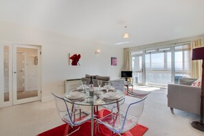 Ein modernes Wohnzimmer mit einem Glastisch, grauem Sofa und einem großen Fenster mit Blick.
