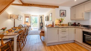 Une cuisine chaleureuse au plancher de bois, un coin repas avec une table mise pour le petit-déjeuner, et une vue sur le jardin par la porte ouverte.