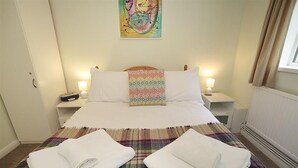 A neatly made bed with a colorful pillow, two bedside tables with lamps, and a painting on the wall. - 1 Bed in Langland (oc-hh147) (Newton)