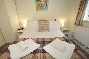 A neatly made bed with a colorful pillow, two bedside tables with lamps, and a painting on the wall. - 1 Bed in Langland (oc-hh147) (Newton)