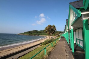 A coastal walkway with a beach, a green building with white trim, and a hill in the background. - 1 Bed in Langland (oc-hh147) (Newton)