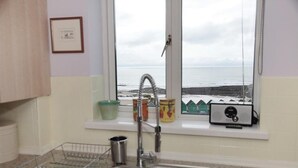 A kitchen with a sink, a window overlooking the sea, and a radio on the windowsill. - 1 Bed in Langland (oc-hh147) (Newton)