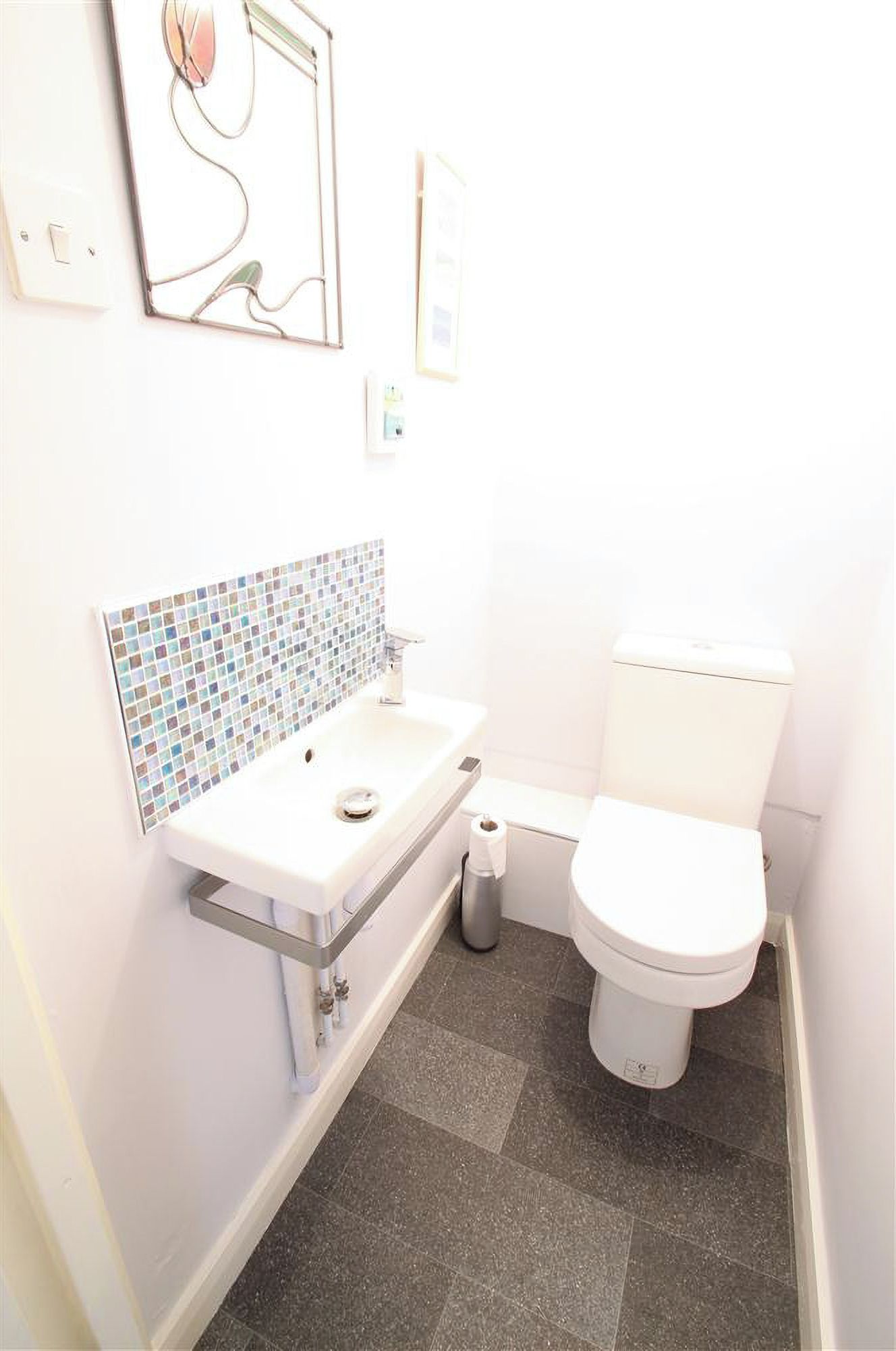 A small, white bathroom with a tiled sink, a toilet, and a trash can.
