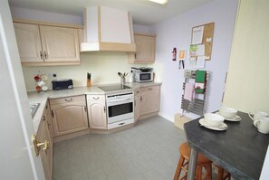 Una cocina compacta con armarios de madera clara, un microondas, un tostador y un lavamanos. Hay una pizarra en la pared y un tablón de anuncios con papeles.