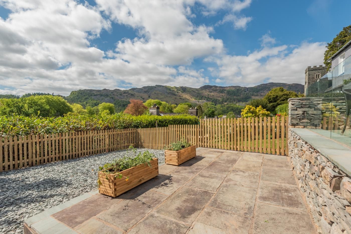 A patio with stone flooring, wooden planters, and a wooden fence.