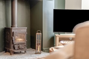 A room with a wood-burning stove, a television, and a small table with a candle. - 2 Bed in Chapel Stile (oc-u32104) (Chapel Stile)
