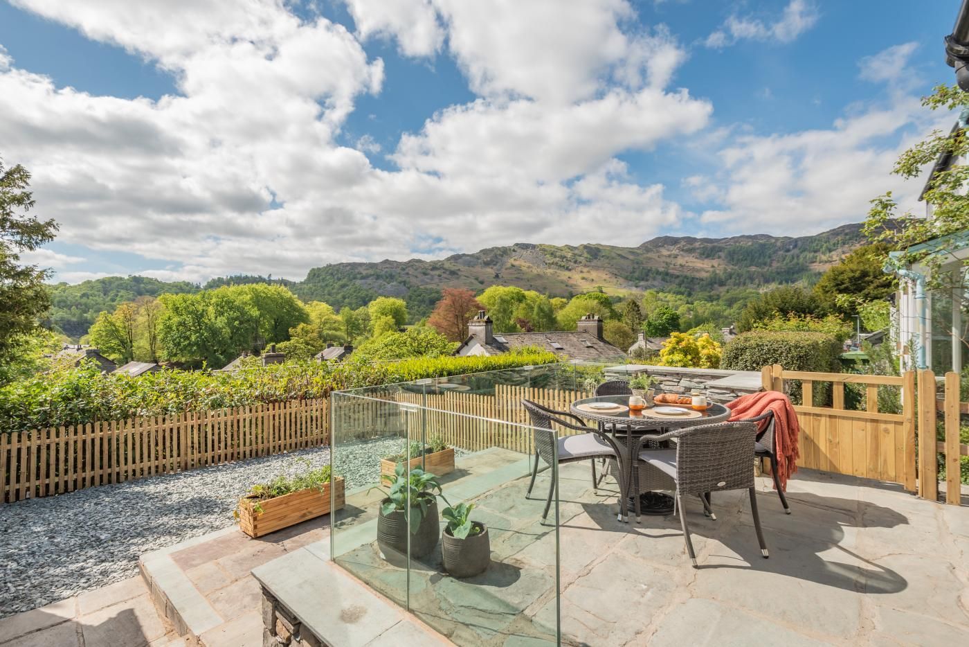 A patio with a glass enclosure, outdoor furniture, and a view of a village and hills.