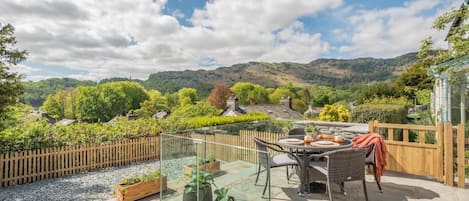 A patio with a glass enclosure, outdoor furniture, and a view of a village and hills.