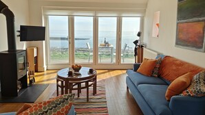 A cozy living room with a blue sofa, a round wooden table, and a large window offering a view of the sea. - 2 Bed in Craster (oc-c25099) (Dunstan)