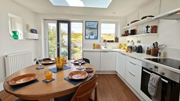 A modern kitchen with a skylight, a dining area with a round table, and a view of the countryside through large windows. - 2 Bed in Craster (oc-c25099) (Dunstan)