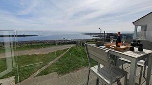 A balcony with a table set for two, overlooking a coastal landscape with a view of the sea and distant land. - 2 Bed in Craster (oc-c25099) (Dunstan)