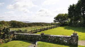 A stone wall with a wooden fence leading to a grassy area with a stone pathway. - 3 Bed in Overton (oc-hh2103) (Port Eynon)