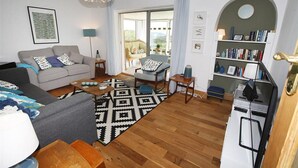 A living room with a grey sofa, a patterned rug, a wooden coffee table, and a bookshelf filled with books. - 3 Bed in Overton (oc-hh2103) (Port Eynon)