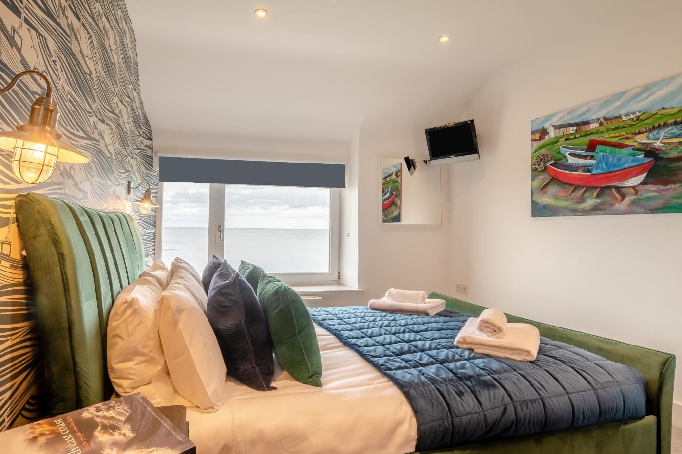 A hotel room with a bed, pillows, a painting, a television, and a view of the sea.