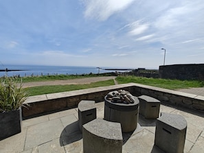 A stone seating area with a fire pit, overlooking a coastal path and the sea. - 3 Bed in Craster (oc-c25115) (Dunstan)