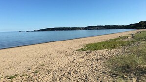 En sandstrand med stilla vatten och en klar himmel.