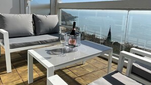 A balcony with a white sofa, a glass table, and a bottle of champagne.
