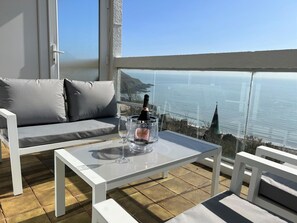 A balcony with a white sofa, a glass table, and a bottle of champagne.