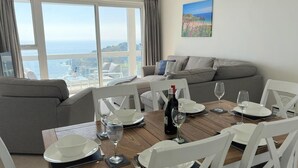 A dining area with a wooden table set for four, white chairs, and a view of the city through large windows.