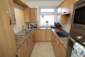 A compact kitchen with wooden cabinets, a granite countertop, a stainless steel sink, a stove, and a window with a plant.