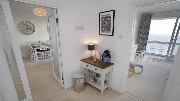 A room with a wooden console table, a lamp, a framed picture, a globe, a mirror, and a view of the ocean through a large window.