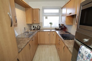 A compact kitchen with wooden cabinets, a granite countertop, a stainless steel sink, a stove, and a window with a plant. - 2 Bed in Langland (oc-hh1426) (Newton)