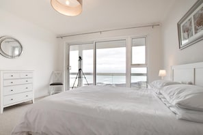 A bedroom with a large bed, a tripod, a chair, and a view of the sea through large windows. - 2 Bed in Langland (oc-hh1426) (Newton)
