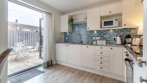 Ett modernt kök med vita skåp, en blå väggbeklädnad bakom arbetsbänken och en skjutdörr i glas som leder ut till en uteplats.