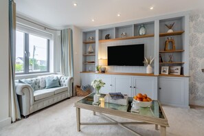 A living room with a sofa, a glass coffee table, and a TV mounted on a wall with built-in shelving. - 1 Bed in Southwold (oc-s32059) (Southwold)