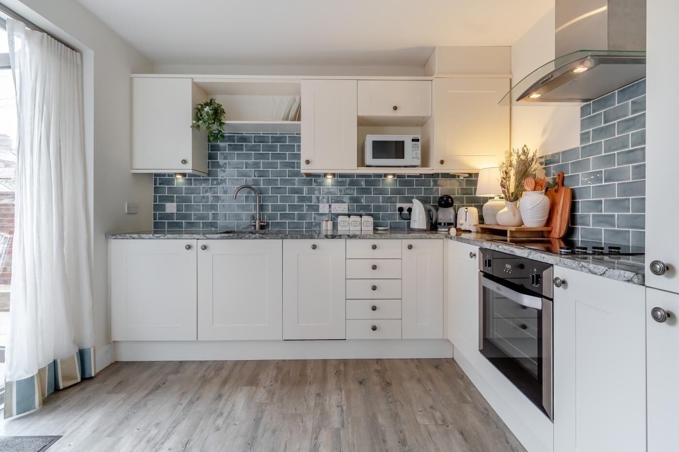 Una cocina moderna con armarios blancos, microondas, estufa y salpicadero de azulejos.