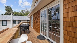 A wooden deck with a table and chairs, a sliding glass door, and a view of the surrounding area. - The Augustine Suite l Heated Pool  l Walk to DNTN (St. Augustine)