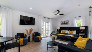 A modern living room with a sofa set, a dining table, and a TV mounted on the wall. - The Augustine Suite l Heated Pool  l Walk to DNTN (St. Augustine)