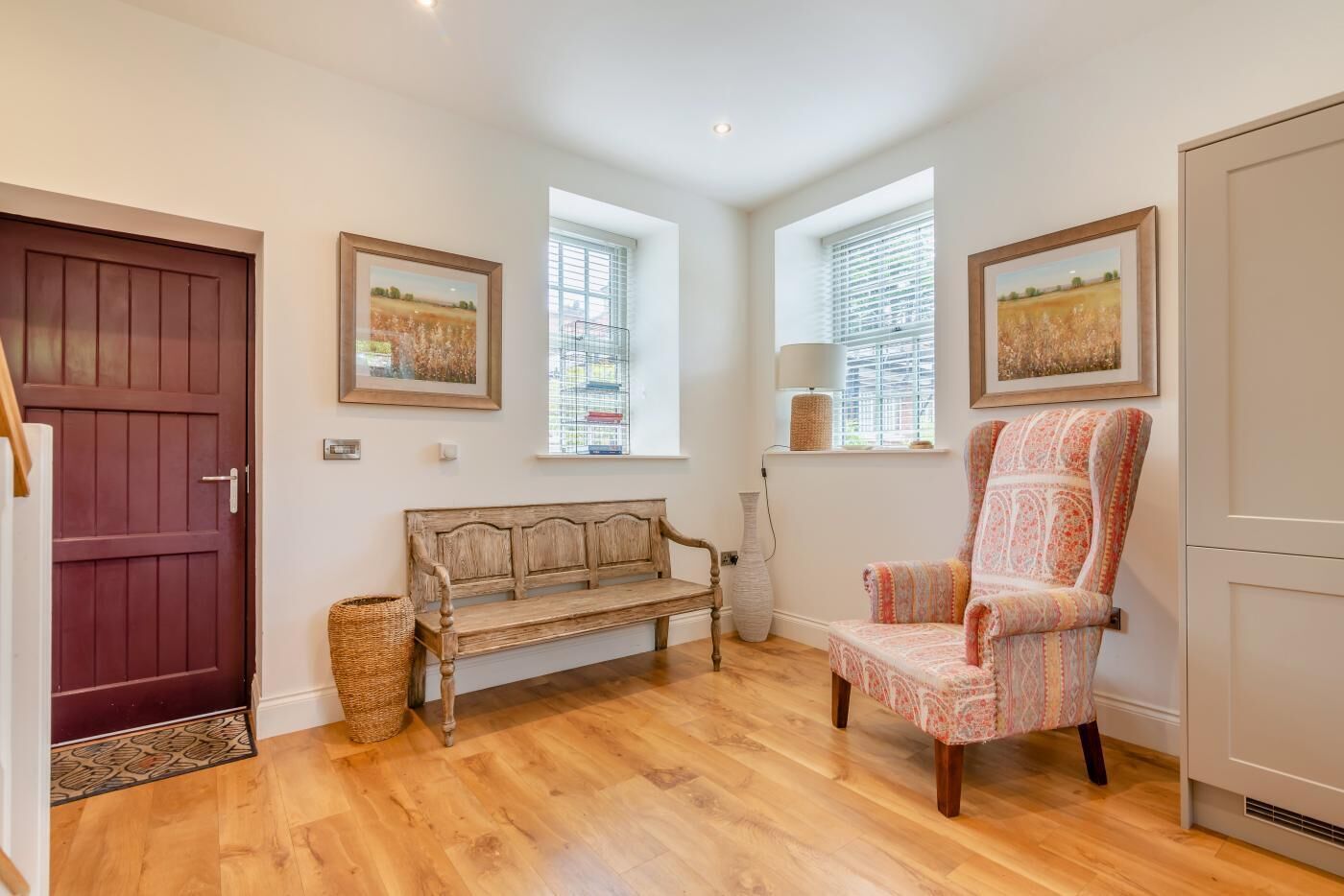 A cozy room with a wooden bench, a patterned armchair, and two windows with blinds.