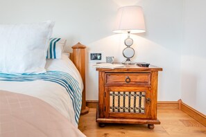 Ein Schlafzimmer mit einem Bett, einem Nachttisch mit Lampe, einem kleinen Holzschrank und einem Beistelltisch mit Bilderrahmen.