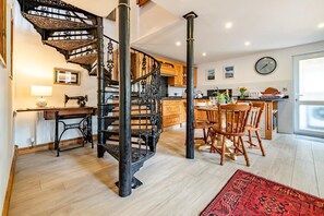 A kitchen with a spiral staircase, wooden cabinets, a dining table with chairs, and a red patterned rug. - 2 Bed in Jeffreyston (oc-pw9167) (Jeffreyston)