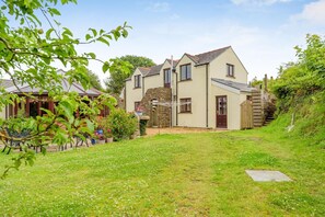 A two-story house with a stone wall, a wooden staircase, and a garden with a lawn and potted plants. - 2 Bed in Jeffreyston (oc-pw9167) (Jeffreyston)