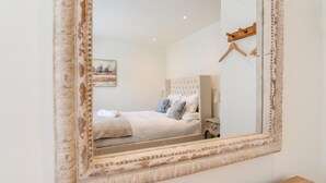 Una camera da letto con un grande specchio, un letto con lenzuola bianche, una testiera e un comodino.