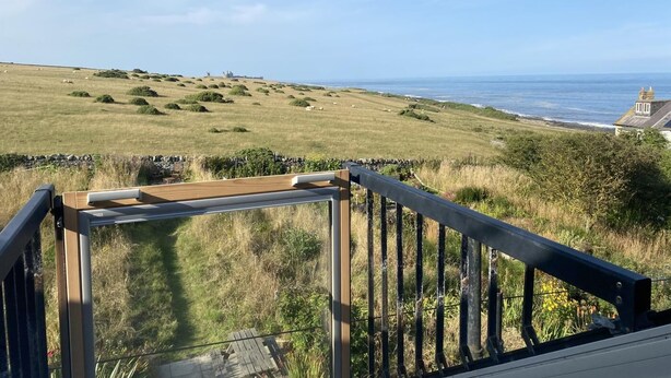 Een schilderachtig uitzicht vanaf een balkon met glazen dak, over een grasland en de zee.