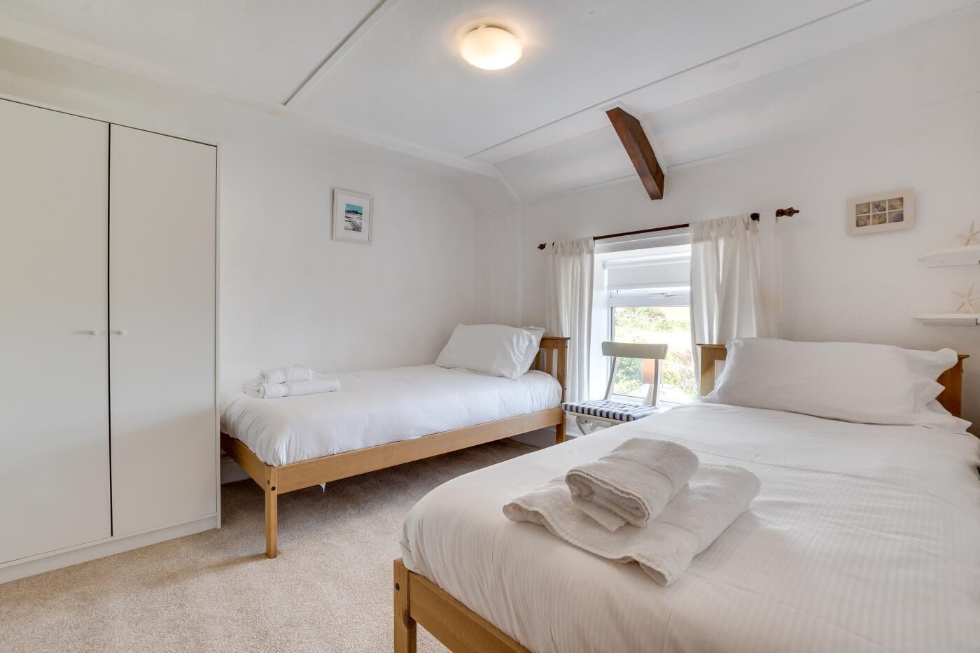 A bedroom with two single beds, a wardrobe, and a balcony with a chair.