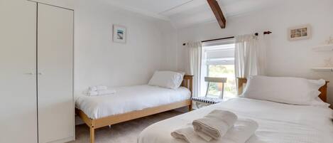 A bedroom with two single beds, a wardrobe, and a balcony with a chair.