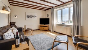 Una sala de estar con un sofá, una mesa de centro, un televisor y una ventana con cortinas.
