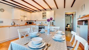 Een moderne keuken met witte kasten, een eettafel gedekt met borden en bestek, en een houten plafond.