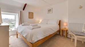 Een slaapkamer met een houten bed, witte beddengoed, een nachtkastje met een lamp, een stoel en uitzicht op het buiten.
