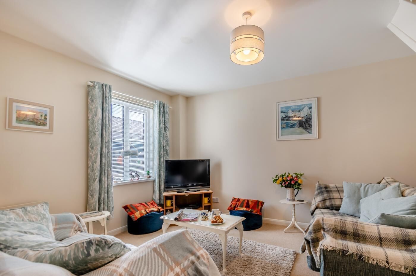 A cozy living room with a flat-screen TV, comfortable seating, a coffee table, and artwork on the walls.