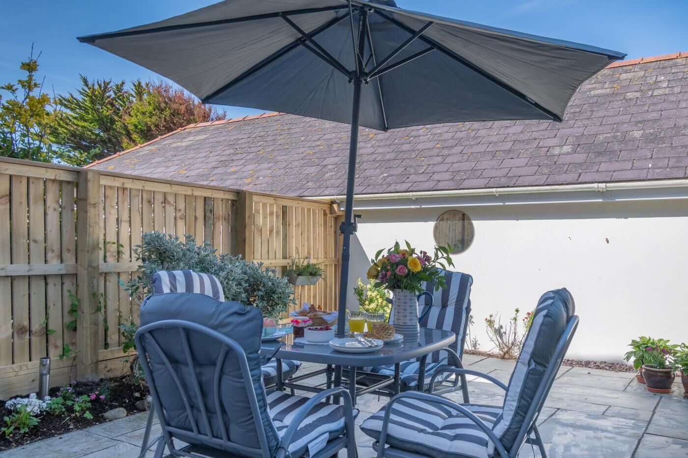 An outdoor patio with a round table, four chairs, a large umbrella, and a wooden fence.