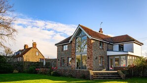 A two-story house with a stone facade, large windows, and a well-maintained lawn. - 4 Bed in Blakeney (oc-2070) (Blakeney)