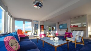 A modern living room with a blue carpet, a coffee table, and colorful furniture. - 4 Bed in Blakeney (oc-2070) (Blakeney)