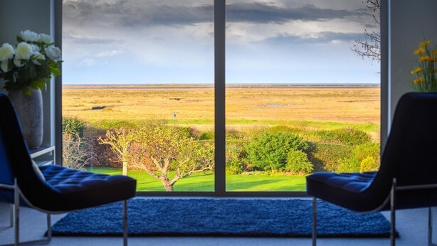 A room with two chairs facing a large window overlooking a grassy landscape. - 4 Bed in Blakeney (oc-2070) (Blakeney)