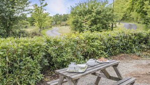 A picnic table with a tray of food and a teapot in a park with a winding path and greenery.